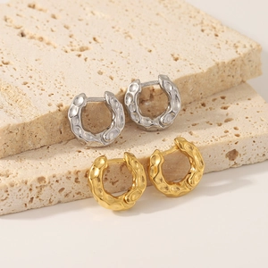 Lava texture C-shaped hoop earrings in gold and silver finish on travertine stone