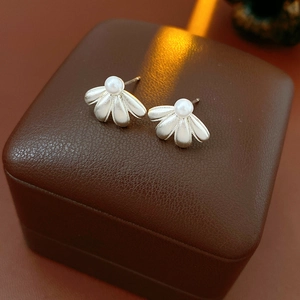Detailed view of silver petal earrings with white pearl centers on brown leather gift box