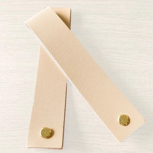 Detail of beige PU leather straps with golden snap buttons on light wood background