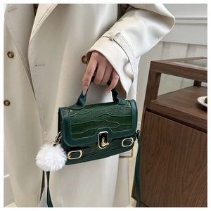 Detail of emerald green crocodile texture bag with gold lock and white fur ball charm