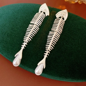 Detailed close-up of silver fishbone earrings with pearls on dark green velvet
