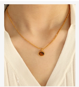 Dettaglio della collana a catena dorata con ciondolo in pietra naturale marrone su modella