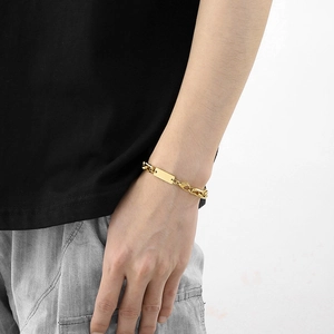 Detail of a gold stainless steel rectangle tag bracelet with a lobster clasp on a wrist