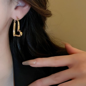 Close-up of minimalist gold heart hoop earring on a model in warm indoor light