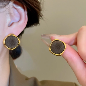 Close-up of geometric gold and black flocking earrings worn by a model in warm light