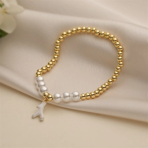 Elegant gold beads and pearl bracelet with white coral pendant on silk background