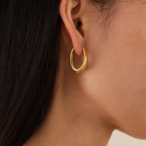 Close-up of a person wearing minimalist high-polish golden U-shaped geometric earrings