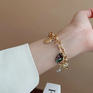 Gold chunky chain bracelet with shell and star pendants worn on a female wrist