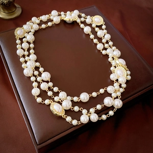 Close-up of layered pearl necklace with gold-tone oval charms on a leather surface