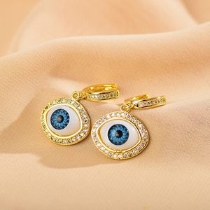 Macro view of gold evil eye earrings with blue enamel and sparkling crystal accents