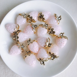 Detail of glittery pink resin strawberry charms with gold leaf accents on a ceramic plate