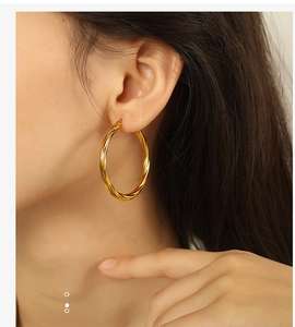 Close-up of a model wearing a textured gold twisted hoop earring with a polished finish