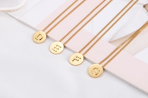 Detail of four gold-plated round alphabet necklaces with letters D, E, F, and G