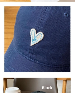 Detailed close-up of white heart embroidery with blue letter B on a black baseball cap