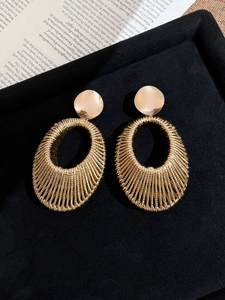 Detail of gold woven oval drop earrings resting on black velvet and newspaper backdrop