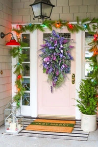 Detailed view of teardrop lavender tulip wreath hanging on a pink door with festive lights