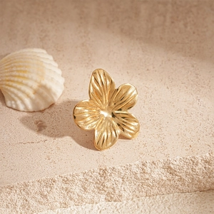 Golden metal flower clip-on earring on a stone background with a natural seashell