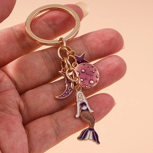 Golden mermaid keychain with purple moon and star enamel pendants held in hand