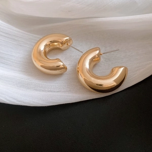 Detailed view of chunky golden C-shaped hoop earrings on elegant white draped fabric