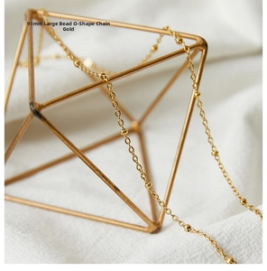 Close-up of golden beaded cable chain necklace draped on a gold geometric display stand