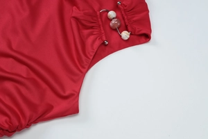 Dettaglio della trama del top rosso con perline marmorizzate e anello metallico decorativo