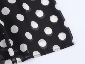 Detailed macro view of black chiffon fabric with white polka dots and stitched hem