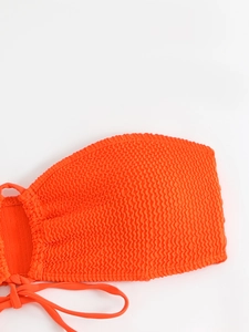 Detail of bright orange smocked bikini fabric with elastic texture and ruched finish