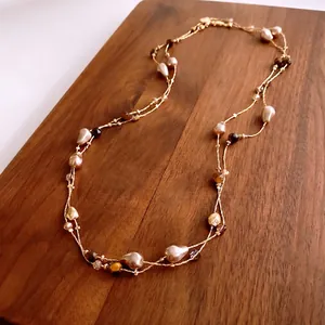 Elegant gold layering necklace with baroque pearls and tiger eye beads on wood surface