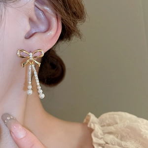 Close-up of gold bow earrings with pearls and crystals worn on an elegant model