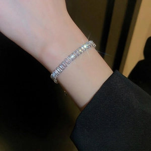 Bracelet rivière argenté avec zircons rectangulaires porté sur un poignet en veste noire