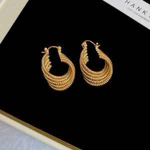 Detail of gold twisted rope hoop earrings featuring multi-layer woven texture on black velvet