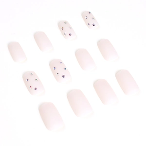 Matte nude pink press-on nails set with sparkling rhinestones on white background