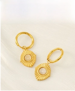 Detail of 18K gold-plated earrings with cat eye stone pendant on white silk fabric