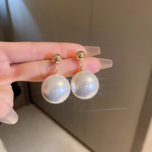 Close-up of gold-plated pearl drop earrings with large white pearls held by hand