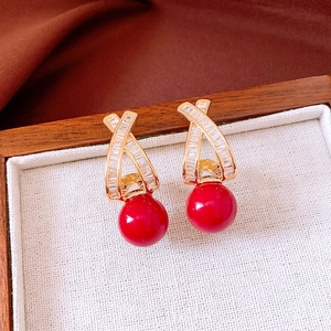 Close-up of 18k gold plated earrings featuring zircon stones and a large red pearl drop