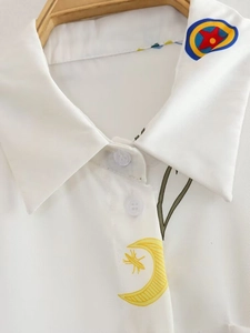 Détail du col d'une chemise blanche avec imprimé lune jaune et badge coloré sur cintre