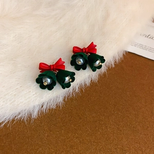 Dettaglio di orecchini a fiocco rosso e mughetto con perle su sfondo di peluche