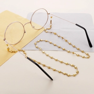 Chaîne de lunettes en titane doré avec cœurs et montures rondes vintage sur fond neutre