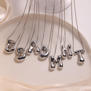 Macro detail of silver puffy alphabet necklaces on white tray with silk fabric