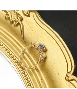 Close-up of handmade gold wire-wrapped ring with white pearls and purple flower charm