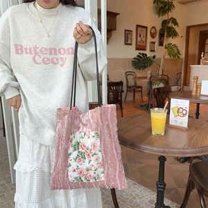 Detail of pink velvet tote bag with pleated texture and floral patch in a cafe setting