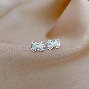 Macro shot of silver bow earrings with pearl inlay on soft champagne silk fabric