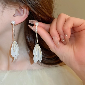 Close-up of long tassel earrings with white pearls, crystals, and delicate acrylic petals