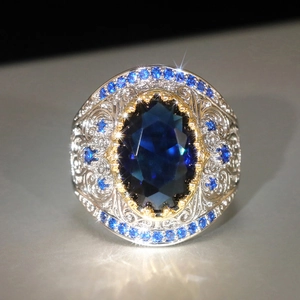 Macro di un anello vintage con gemma blu ovale e incisioni floreali in argento