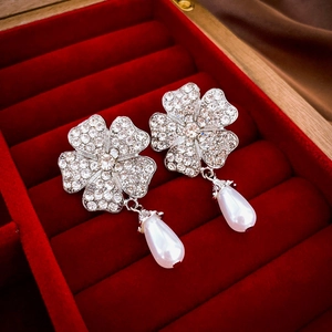 Close-up of silver flower earrings with pavé diamonds and drop pearls on red velvet