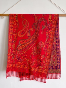 Detail of red paisley faux cashmere shawl scarf with twisted tassels on a wooden bar