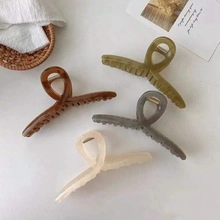 Flat lay of four matte acrylic hair claw clips in amber, green, grey, and beige tones