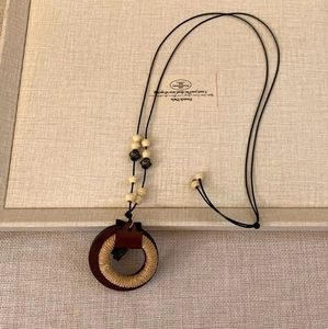 Detail einer Boho-Halskette mit gewebten Holzringen und Naturperlen auf Stoffhintergrund