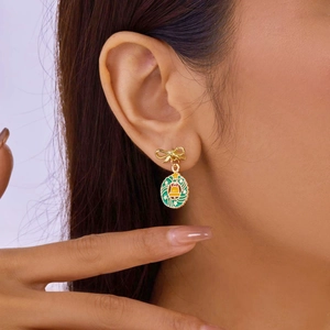 Close-up of festive Christmas wreath earrings with green leaves and a golden bow on model