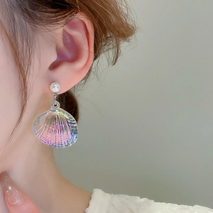 Close-up of iridescent shell-shaped dangle earrings with a white pearl on a female model